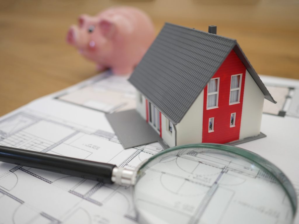 Image of a magnifying glass on blueprints with a piggy bank in the background