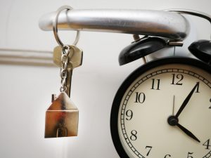 Image of a key on a key chain hanging on a doorknob with a clock in the background