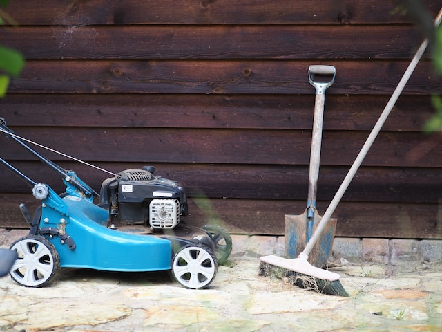 Image of a blue lawn mower next to a shovel and a push broom