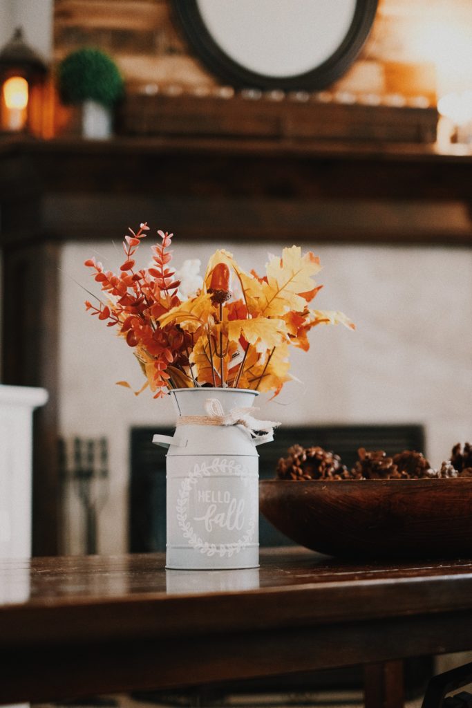 Image of a white vase filled with fall branches and leaves next to a bowl of pinecones