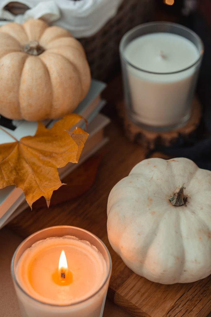 Image of mini white pumpkins next to a lit candle a fall leaf on a coffee table